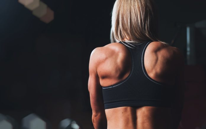 Спортивная девушка в черном топе демонстрирует мышцы спины