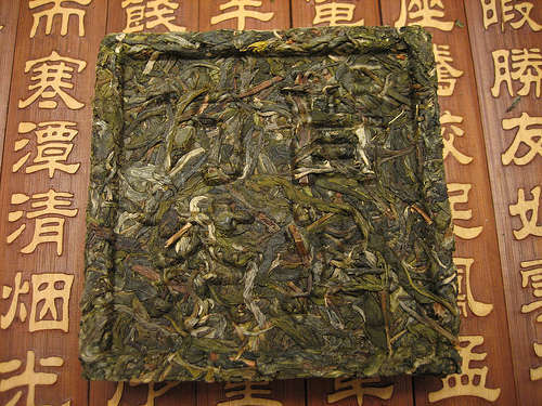 Green tea leaves compressed into a square shape with Chinese characters printed on it, against a wooden background with Chinese characters